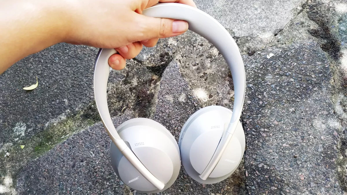 Someone holding the bose 700 headphones in white above pavement