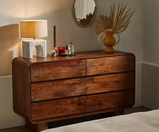 Urban Outfitters wooden dresser with trinkets on top against a gray bedroom wall.