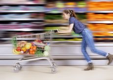 Shop price inflation symbolised by woman running through a supermarket with trolley