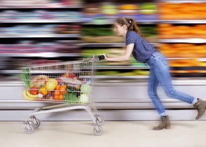 Shop price inflation symbolised by woman running through a supermarket with trolley