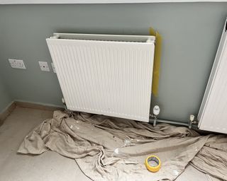 White radiator against green wall with dust sheet and frog tape