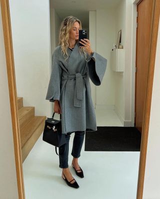 Anouk wears a gray coat, dark wash skinny jeans, black flats, and a black hermes bag.