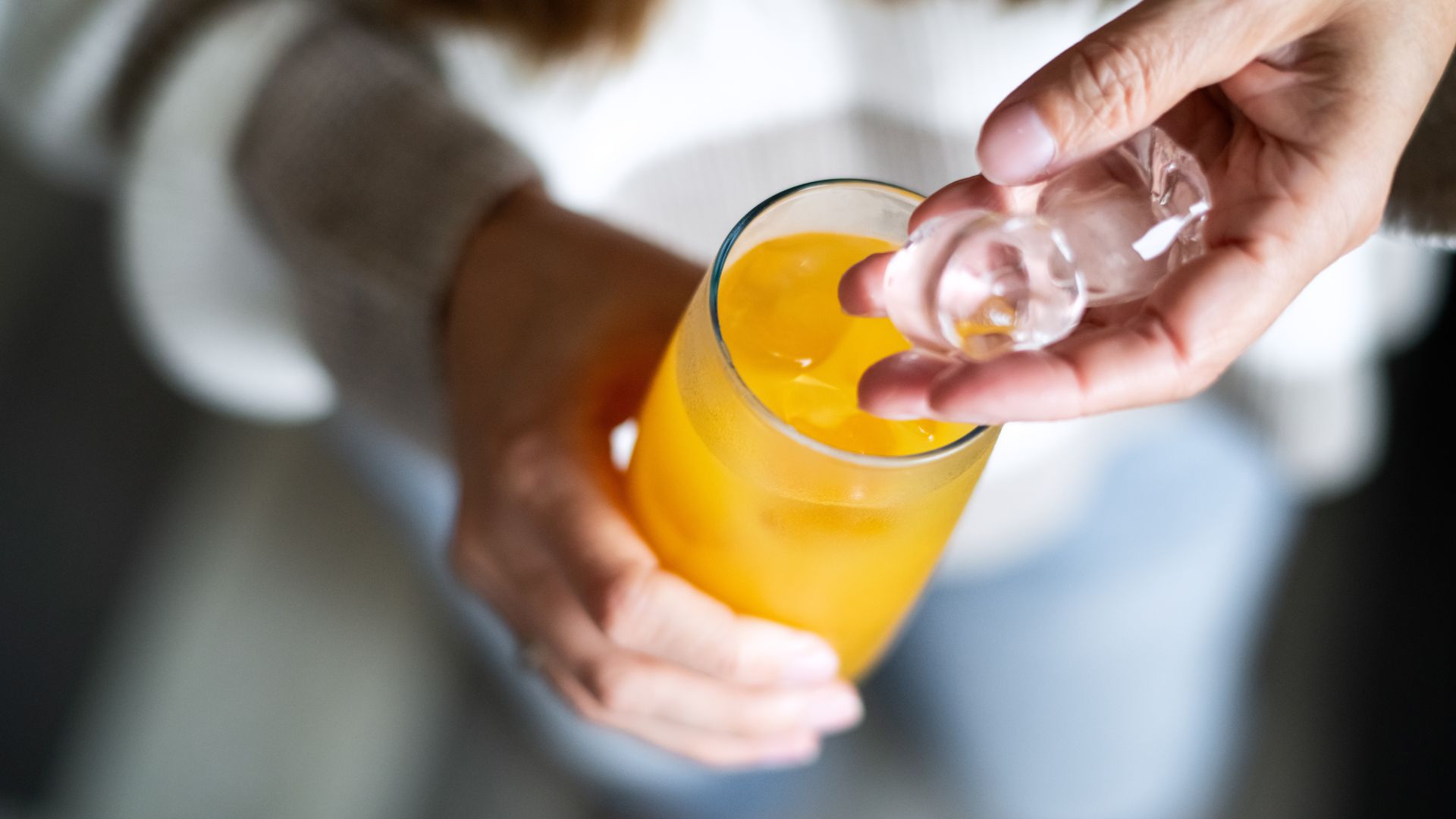 Woman holding glass of orange juice and handful of ice