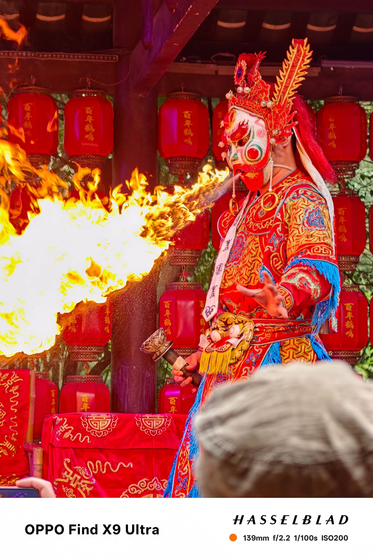 Masked fire-breathing performer in colorful costume with flames bursting outward