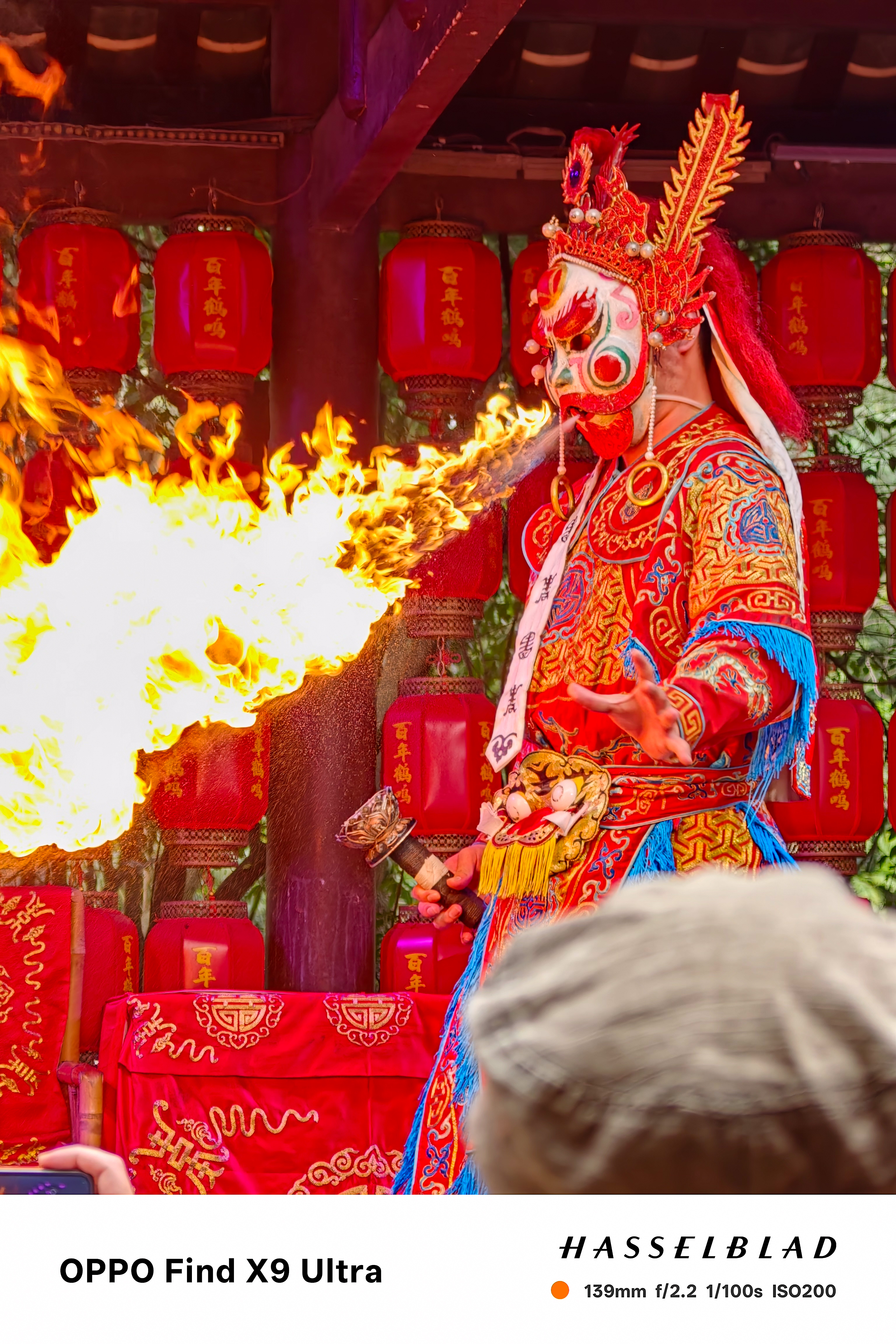 Masked fire-breathing performer in colorful costume with flames bursting outward