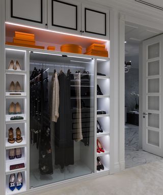 A walk-in closet with shoe storage on the sides and lighting, hat boxes on the top shelf