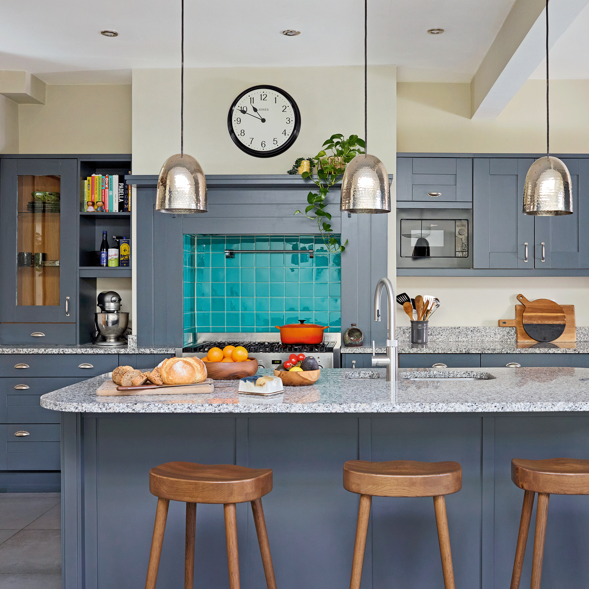 a kitchen with dark grey cabinets and pale walls a bright blue cooker splashback and a sink in the island unit