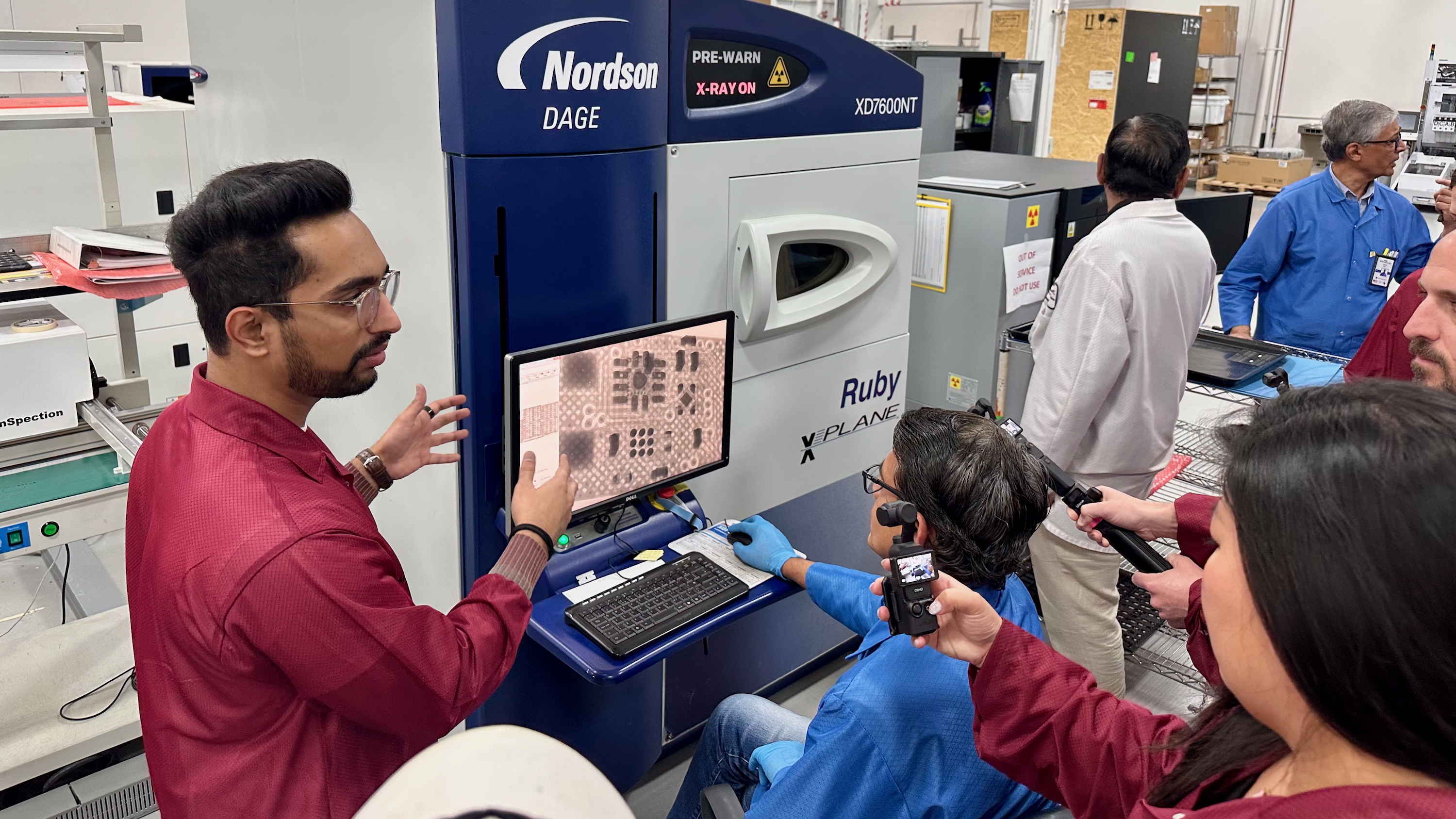 An Ultrahuman factory worker sits outside an X-Ray machine, with a screen showing the internals of a Ring Air PCB so he can check for defects.