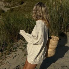 Lucy Williams wearing a cotton loose sweater with a straw bag on the beach.