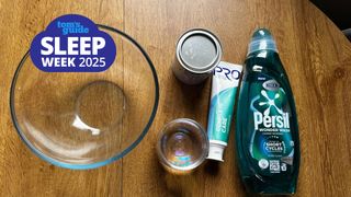 The image shows a glass bowl, a tube of toothpaste, a bottle of liquid laundry detergent and a jar of baking soda on a wooden table