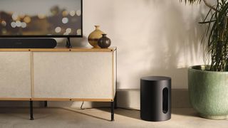 Sonos Sub Mini i sort står på gulvet ved siden af et tv-møbel i en stue