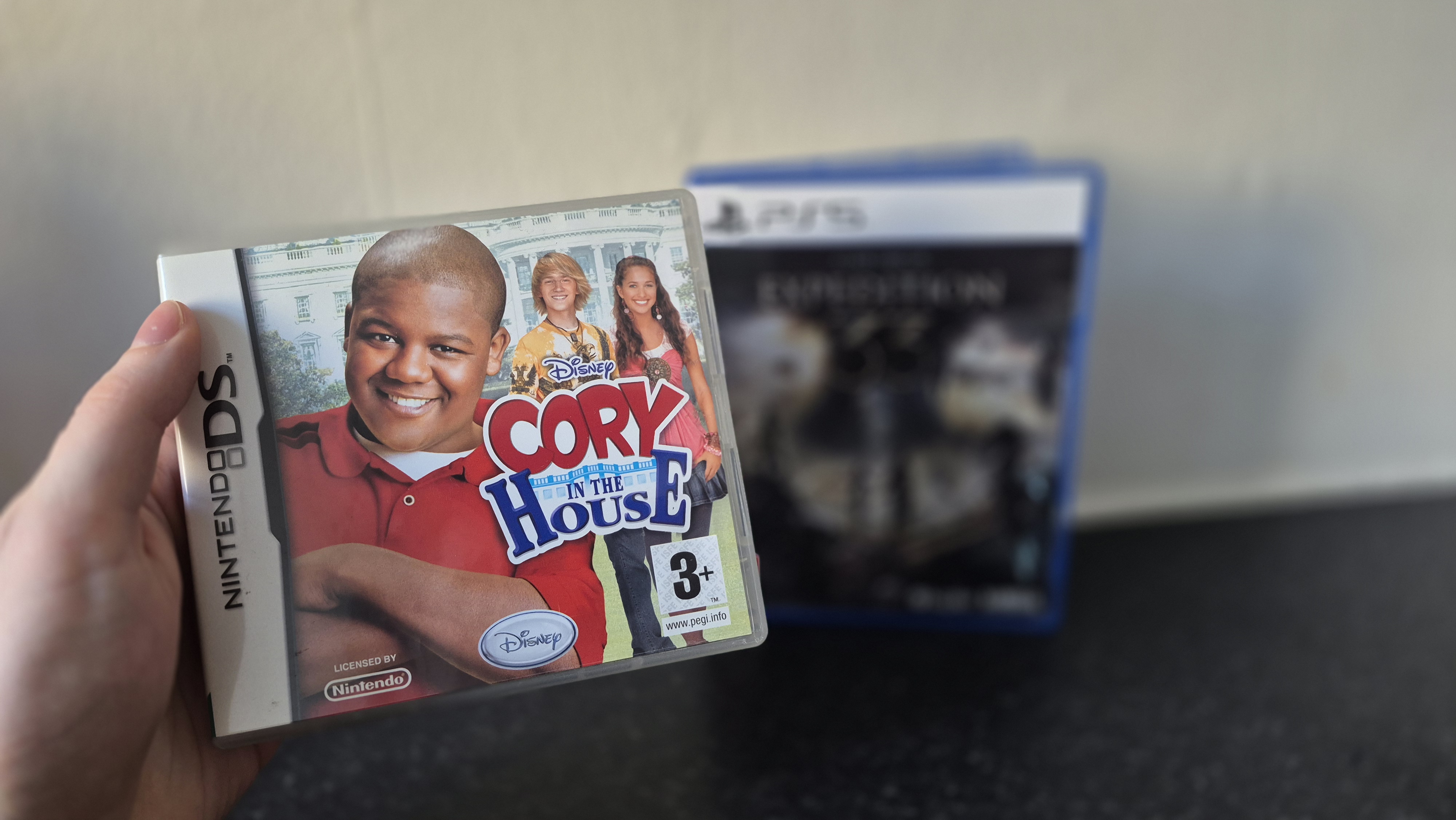 Man holding up Cory in the House for the Nintendo DS game box in front of Clair Obscur: Expedition 33 game box