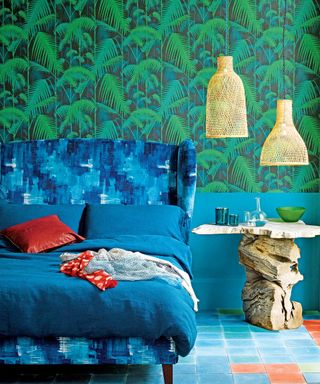 Bold blue and green bedroom, green palm print wallpaper with blue bed, wooden table and natural pendant lights