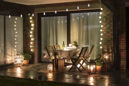 An outside deck at night with an outdoor dining set and string lights