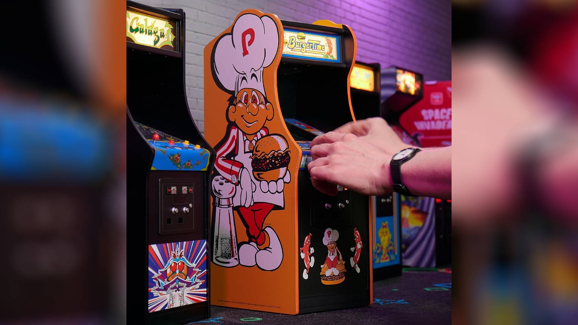 Hands using Quarter Arcades Burger Time machine next to other models.