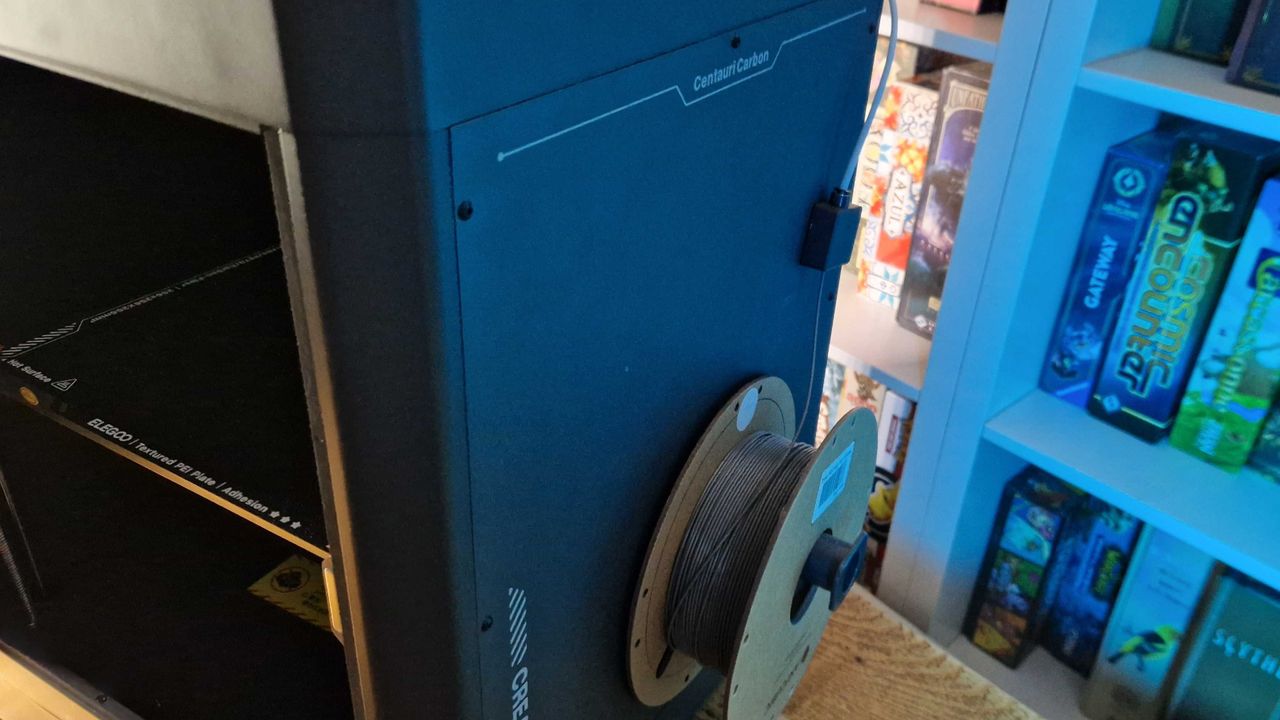 Side of the Elegoo Centauri Carbon with filament, all against a set of board game shelves