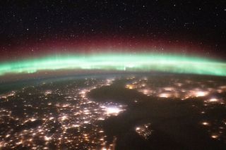 This image, taken from the International Space Station, shows Earth's glowing, colorful aurora alongside lights coming from the cities on our planet's surface down below. When electrically-charged particles from the sun interact with gases in Earth's ionosphere, they create visual displays called auroras.