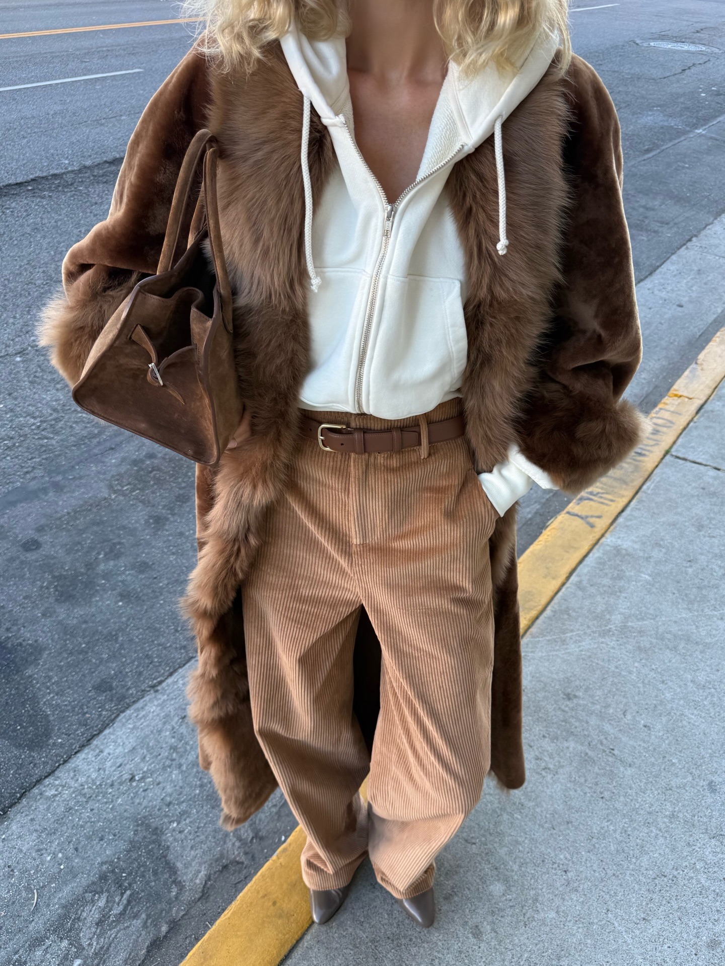 Elsa Hosk wears beige cord trousers with a fur-trimmed coat and a white zip-up hoodie.