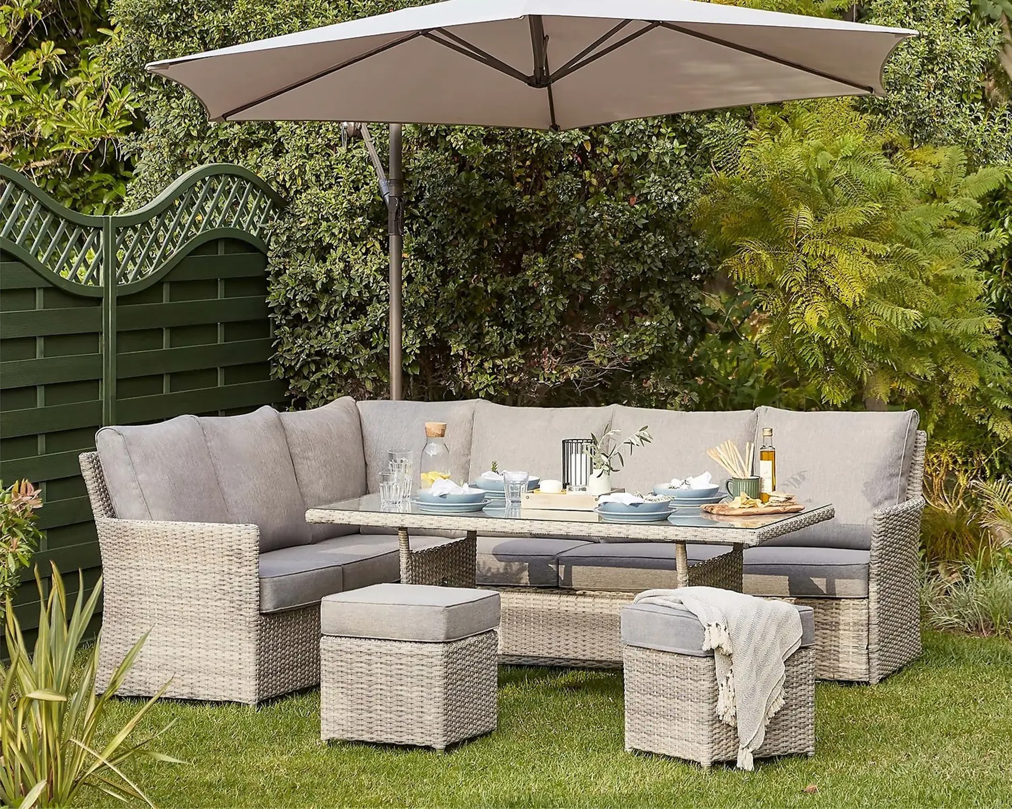 A rattan corner sofa set with an aluminium frame in a garden with an outdoor umbrella