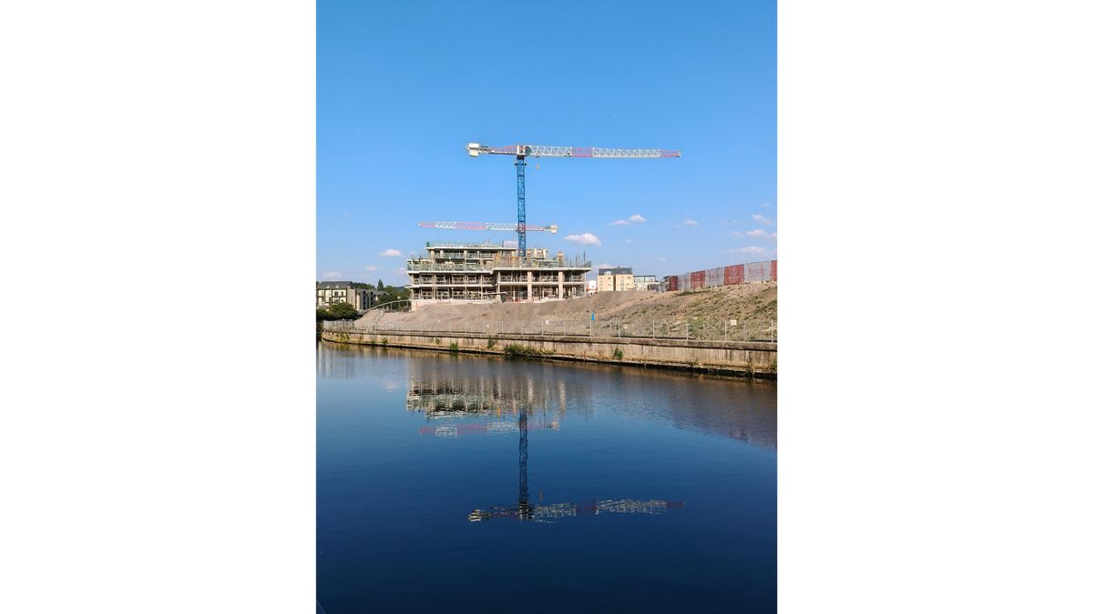 A crane, building site and blue sky reflected in a river