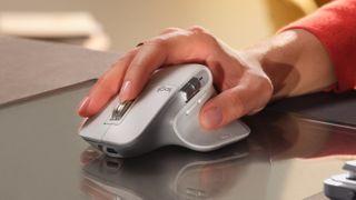 A person's hand holding the Logitech MX Master 3S on a desk.