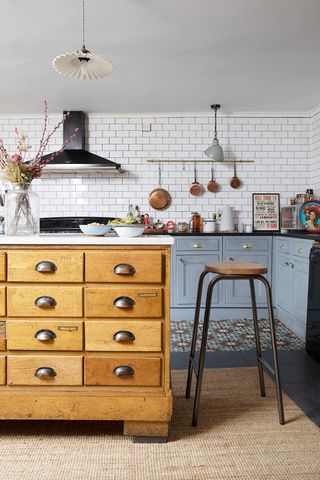 A grey kitchen with wooden drawered cabinet as an island, jute rug, retro tiled flooring and white metro tiled walls