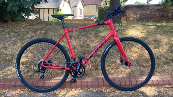 A red Merida Speeder 200 hybrid bike pictured in front of a small green space in a rural market town