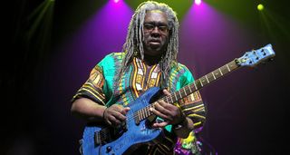 Dwayne Blackbyrd McKnight takes a solo on his blue Framus electric, with purple stage lights in the background.