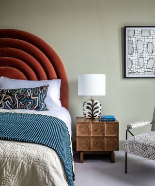 Gray-green bedroom with rust red rounded headboard, wooden side table, bedside lamp