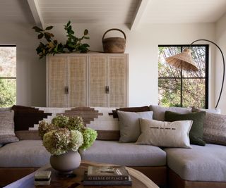 A California modern living room with warm neutral walls and a gray sofa. Earthy colors have been introduced through the decor, and natural materials create a more relaxed atmosphere
