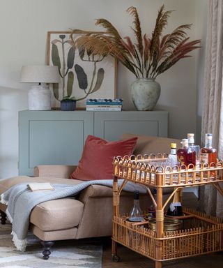 living room with taupe armchair and coral velvet cushion, rattan drinks trolley and eau de nil cupboard