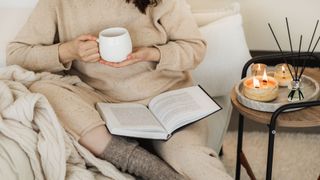 A woman reading with a scented candle burning beside her