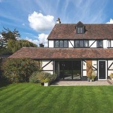 Lush green lawn at the front of a tudor-style detached home.