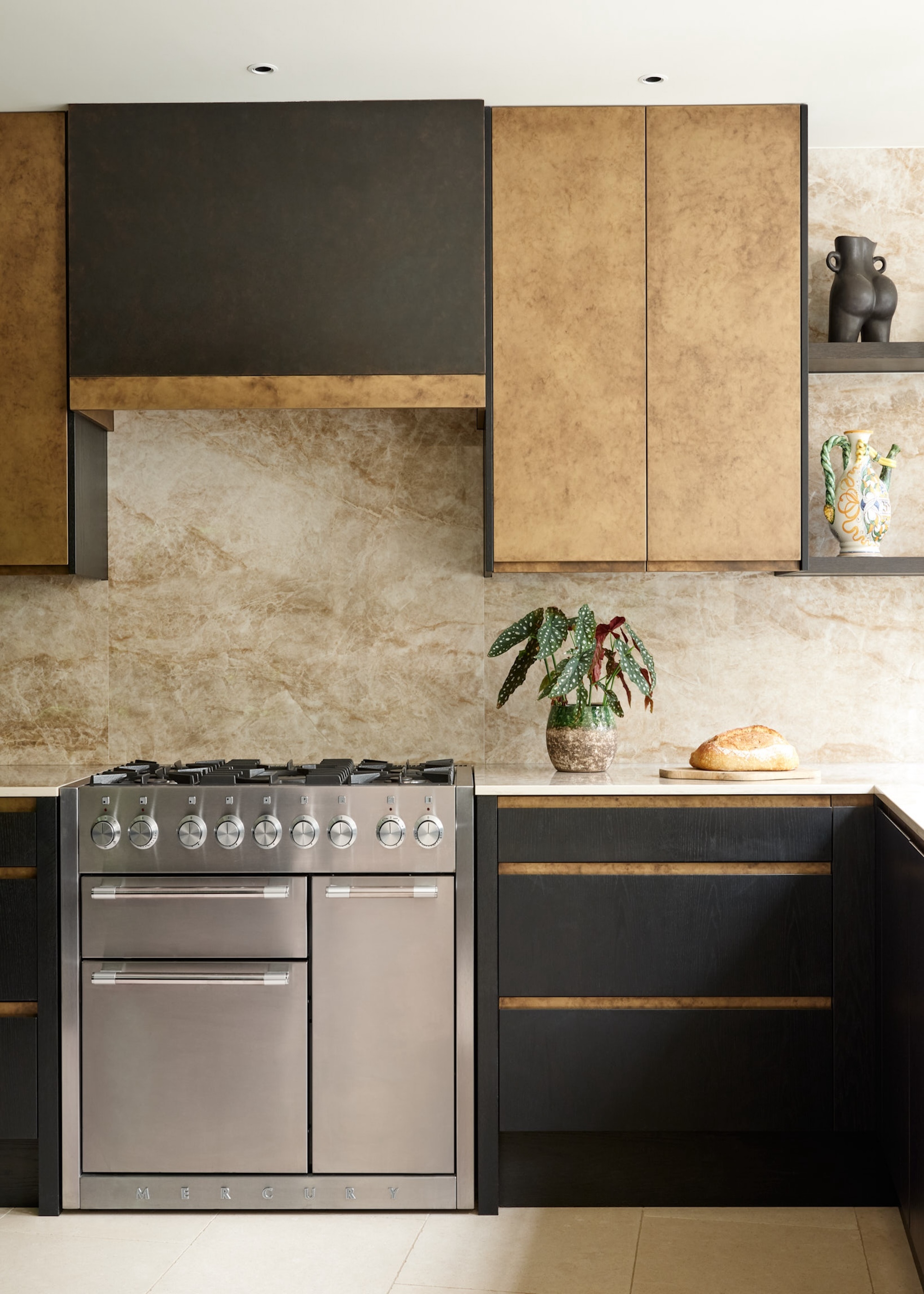 A metallic kitchen with a silver/chrome gas stove as well as a view of open shelving with kitchen decor pieces on top.