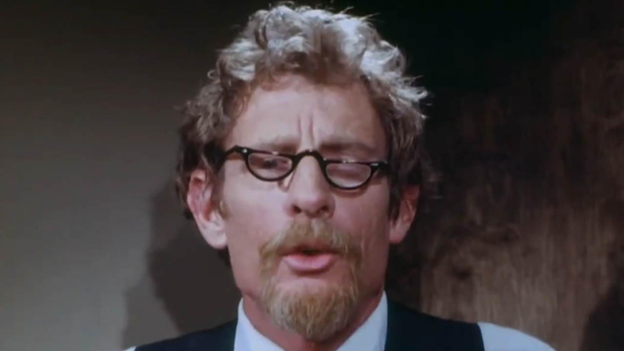 A man with crooked glasses and a beard looking at the camera in Faces of Death