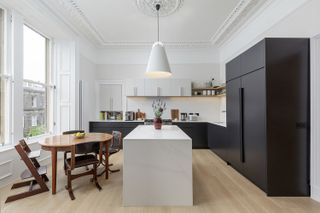 An open plan kitchen with white walls and a smart black L shaped kitchen and mid-century dining table