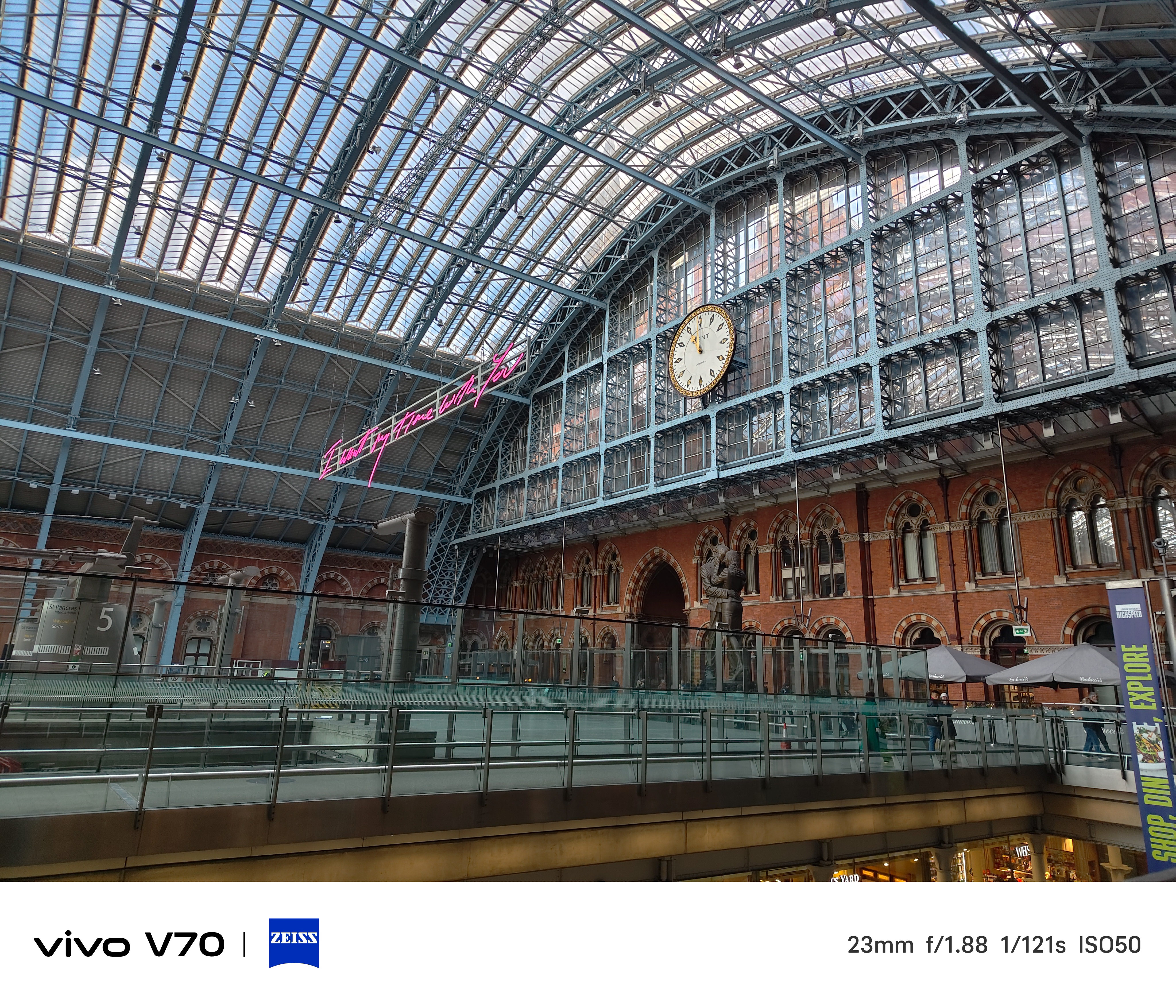 Interior view of St Pancras International concourse with large clock and pink neon sign above.