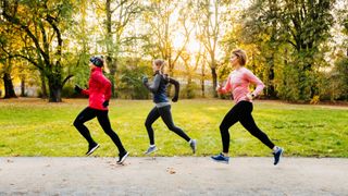 Three women running in a line along a path in a park in the sun