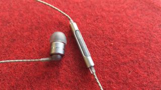 SoundMagic E80D wired in-ear headphones one earbud and inline control on red surface