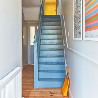 A hallway with a blue-painted staircase and a colourful art prints hanging on the wall