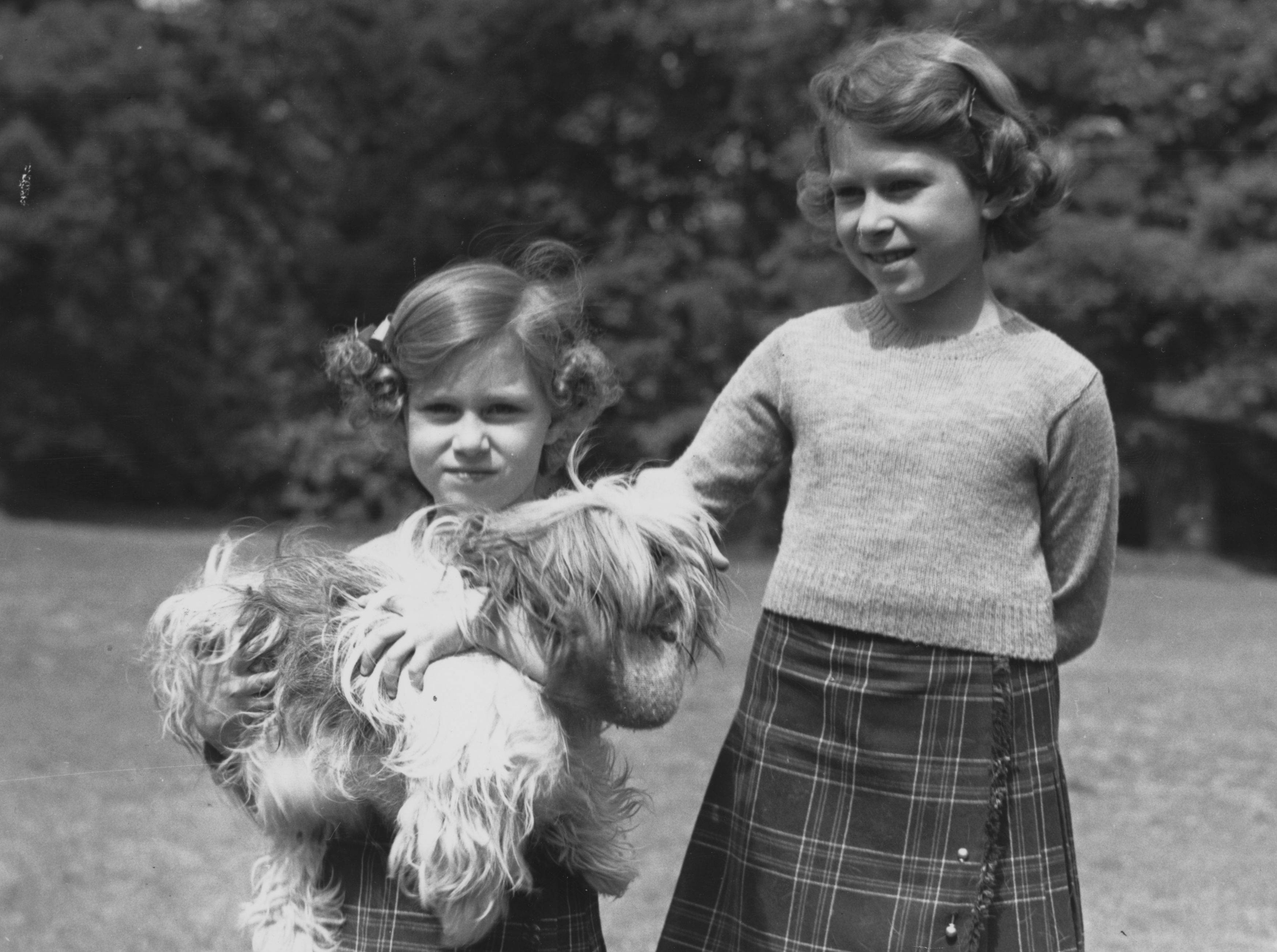 Princess Margaret holding a dog standing next to Princess Elizabeth at Royal Lodge in 1936