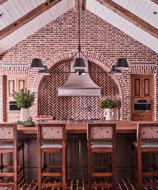 Traditional dining room with beautiful brickwork on walls and flooring, large wooden kitchen island with seating, vaulted ceiling with wooden beams and white paneling