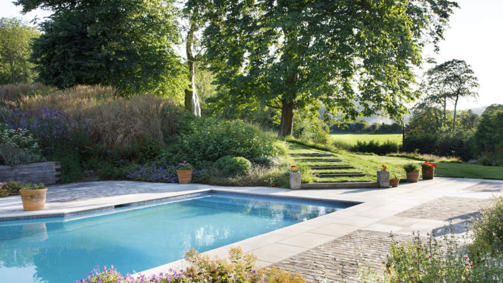 A pool set into a light patio surrounded by lush greenery. 