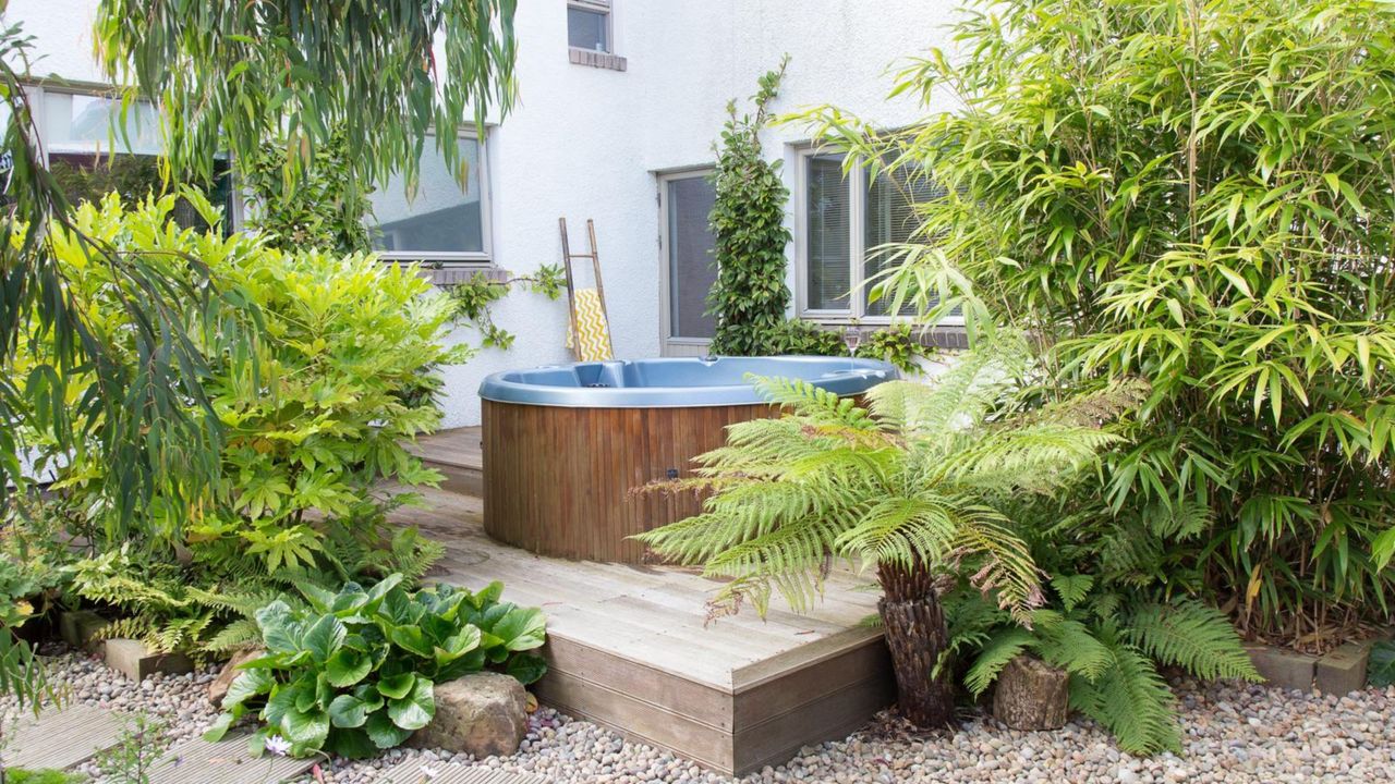 Gravel and decked area with a wooden hot tub surrounded by trees and ferns.