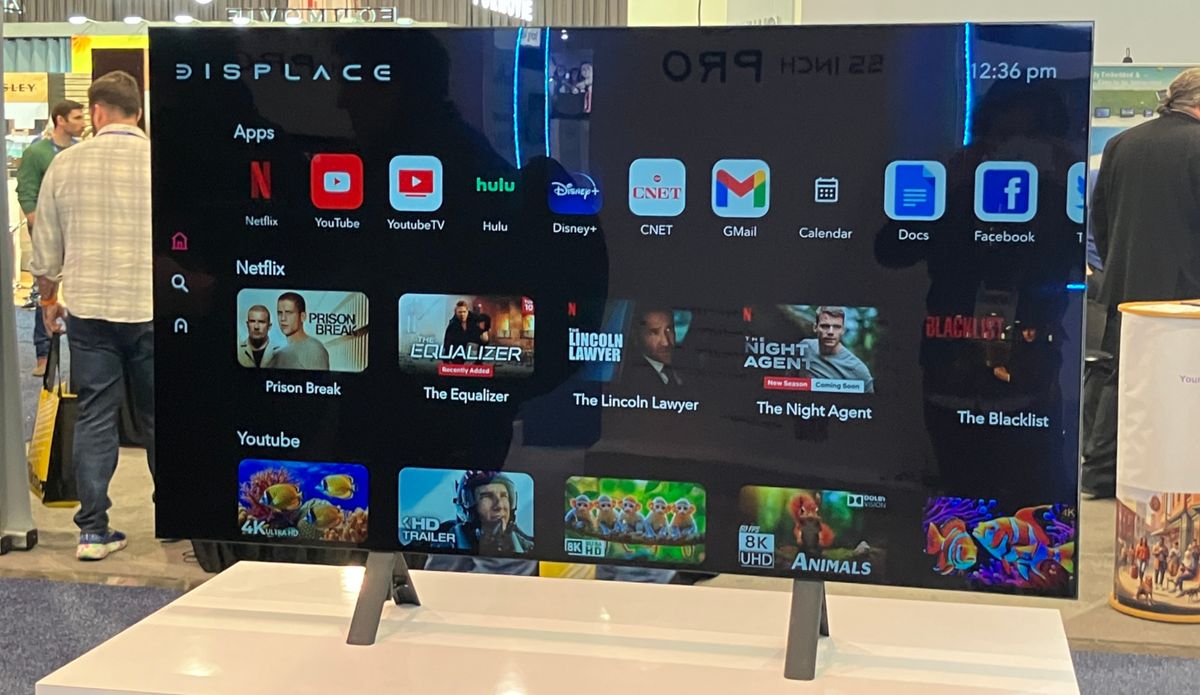 The 55-inch Displace TV sitting on its optional legs at a CES 2025 booth. The TV is displaying a smart platform home screen.