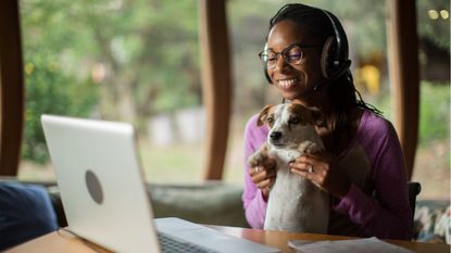 A woman who works from home holds up her dog while on a video call.