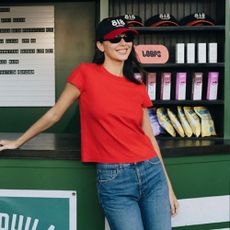 Kendall Jenner poses at a bar wearing dark wash jeans with white Derby shoes and a red t-shirt.