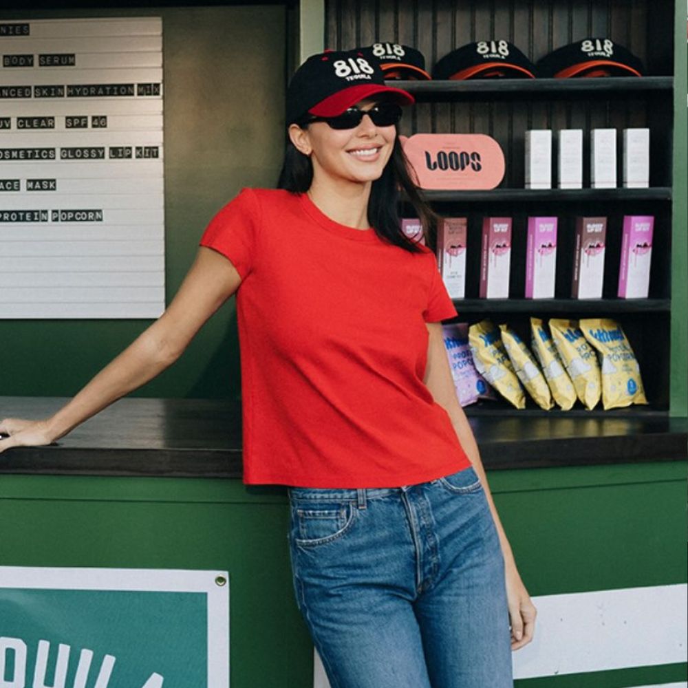 Kendall Jenner poses at a bar wearing dark wash jeans with white Derby shoes and a red t-shirt.