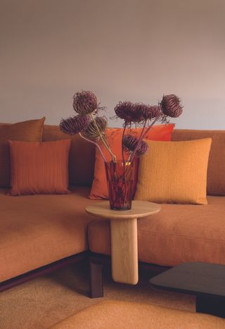 An orange-shaded, autumnal sofa is decorated with just as orangey pillows and flowers.