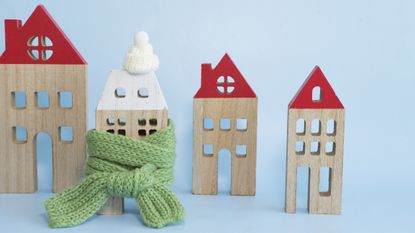 A figurine of a house wrapped in a green scarf next to other houses